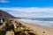 A gorgeous shot of the beach along the coast with vast blue ocean water, large rocks along the beach, silky sand with blue sky