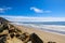 A gorgeous shot of the beach along the coast with vast blue ocean water, large rocks along the beach, silky sand with blue sky