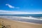 A gorgeous shot of the beach along the coast with vast blue ocean water, large rocks along the beach, silky sand with blue sky