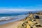 A gorgeous shot of the beach near a long stretch of road with cars and large rocks along the beach, vast blue ocean water