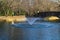 A gorgeous shot of a lake with a water fountain in the park near an arched cobble stone bridge