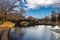 A gorgeous shot of a lake with a water fountain in the park near an arched cobble stone bridge