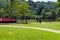 A gorgeous shot of the park with red benches surrounded by lush green trees reflecting off the Chattahoochee river water
