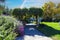 A gorgeous shot of a pergola in the park covered with lush green plants surrounded by colorful flowers and lush green trees