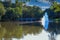 A gorgeous shot of the silky green lake water with a fountain in the middle of the lake with a stone bridge