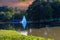 A gorgeous shot of the silky green lake water with a fountain in the middle of the lake with a stone bridge