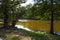 A gorgeous shot of the still brown lake waters with lush green and autumn colored trees and lush green grass on the banks