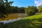 A gorgeous shot of the still brown lake waters with lush green and autumn colored trees and lush green grass on the banks