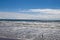 A gorgeous shot of the vast blue ocean water with waves rolling in and birds walking along the beach with blue sky and clouds