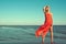 Gorgeous slim blond model in red strapless dress with flying train standing on tiptoe in the sea water