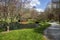 A gorgeous spring landscape in the garden with ponds surrounded by footpaths and lush green trees and grass, red trees