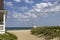 A gorgeous summer landscape at the beach with blue ocean water, silky brown sand, lush green plants and grass, a lifeguard tower