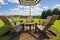 A gorgeous summer landscape at the vineyard with a brown wooden tables and chairs in a circle around a brown and white umbrella