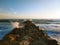 A gorgeous sunset on the beach with ocean waves rolling in and crashing into a jetty made of large rocks at Marina Park Beach