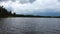 Gorgeous sunset on forest lake view. Lake shore with green trees and plants. Sky covered with heavy thunder clouds.