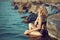 Gorgeous tanned blonde in black swimsuit sitting in the water at the large stones caressing her neck with closed eyes