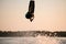 gorgeous view of athletic man doing flip trick in the air on wakeboard against the sunset sky