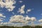 Gorgeous view of blue sky with white clouds over tops of forest trees on summer day.