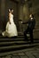 Gorgeous wedding couple bride and groom standing on staircase in front of historical church doorway and serving bouquet