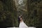Gorgeous wedding couple kissing in winter snowy park. stylish bride in coat and  groom embracing under green trees in winter