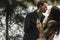 Gorgeous wedding couple kissing in winter snowy park. stylish bride in coat and  groom embracing under green trees in winter