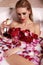 gorgeous woman with blond hair relaxing in bathroom with rose petals, drinking champagne