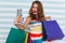 Gorgeous woman with red lips making selfie on striped background. Attractive female shopaholic taking picture of herself