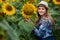 Gorgeous, young, adorable, female farmer standing near a sunflower with a smiley face, in the middle of a beautiful golden