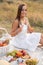 Gorgeous young brunette girl in a white sundress enjoying a picnic in a picturesque place. Romantic picnic