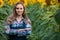 Gorgeous, young, energetic, female farmer standing in the middle of a beautiful green and golden sunflower field