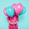 Gorgeous young woman in party outfit holding bunch of colourful balloons, isolated over pastel blue colored background. Birthday.