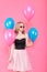 Gorgeous young woman in party outfit holding bunch of colourful balloons, isolated over pastel pink background. Birthday Party.