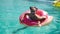 Gorgeous young woman with sunglasses in black bikini lying in inflatable pink donut float in pool on sunny summer day