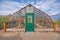 Gothic arch greenhouse with glass panel and green door below the stainless ventilation at Tucson, AZ