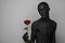 Gothic and Halloween theme: a man with black skin holding a red rose, black death isolated on a gray background in studio