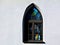 Gothic shape church window with pointy arch and colorful glass in white stucco wall