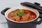 Goulash in a black cocotte with marjoram on white wood