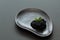 Gourmet. Black salty caviar sterlet decorated with mint leaves on black ceramic plate of unusual shape on black background.