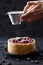 Gourmet dessert. Woman hands pouring icing sugar on small lingonberry pie with frozen raspberries and currants on black background