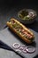 Gourmet dirty hot dog sandwich with various garnish on black slate background. Healthy option of fast food