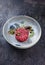 Gourmet tartar raw from beef filet with capers and amarena cherry with truffle cream and lettuce on a Nordic design plate