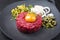 Gourmet tartar raw from beef fillet with yellow of the egg and gherkin with capers and onion rings on design plate