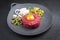 Gourmet tartar raw from beef fillet with yellow of the egg and gherkin with capers and onion rings on a modern design plate