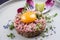 Gourmet tartar raw from beef fillet with yellow of the egg and vegetable on modern design dish