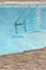 Grab bars ladder in the blue swimming pool. Curved side of a swimming pool with stairs. vertical photo
