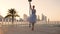 Graceful ballerina with blue dress dancing in Dubai park near the fountain on the sunset view. Diligent ballet dancer