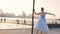 Graceful ballerina in blue dress dancing in park near the fountain on the sunset view.