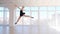 Graceful ballerina dancer performing a jump in white studio