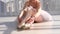 Graceful ballet dancer in tutu sitting on the floor and tying pointe shoes