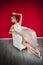 The graceful beauty reclining in a white armchair on a red background. A girl in a short wedding dress poses elegantly